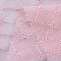 Gros plan sur le Tissu voile froissé au mètre de Longan Craft France, un voile de polyester brodé rose pâle avec des motifs floraux vintage et des bords festonnés, idéal pour confectionner des vêtements ou des rideaux d'été.