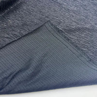 Un gros plan du Tissu lamé froissé au mètre de Longan Craft France, un tissu métallique en polyester brillant destiné aux costumes et à la couture, montre sa surface texturée foncée ; un bord plié révèle le motif quadrillé unique de l'envers.