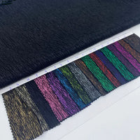Un tissu lamé noir froissé au mètre de Longan Craft France est présenté au-dessus d'échantillons de tissus numérotés en or, bleu, rose, vert, rouge et violet - idéal pour les costumes, les robes et la couture.