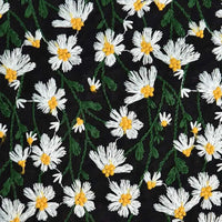 Gros plan sur le "Tissu ramie marguerite au mètre" de Longan Craft France, qui montre des fleurs brodées blanches et jaunes avec des tiges vertes sur un tissu doux en coton-ramie noir, idéal pour les robes, les rideaux ou les projets de couture créatifs.