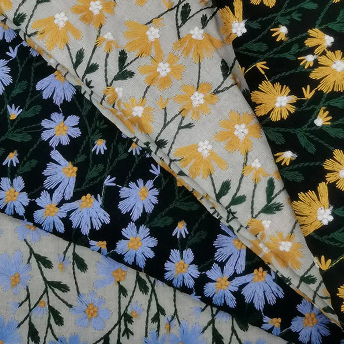 Trois pièces superposées de "Tissu ramie Marguerite au mètre" de Longan Craft France présentent des fleurs brodées jaunes et blanches sur fond beige, des fleurs jaunes et blanches sur fond noir, et des fleurs bleues et jaunes sur fond beige.