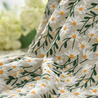 Gros plan sur le tissu ramie marguerite au mètre de Longan Craft France, un doux tissu brodé en coton-ramie avec des marguerites blanches et jaunes et des tiges vertes, idéal pour les peignoirs, les rideaux, la couture ou le bricolage créatif. Des fleurs jaune pâle se fondent dans l'arrière-plan.