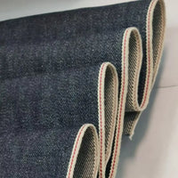 Gros plan sur le tissu en jean selvedge bleu profond 14 oz, 100 % coton, de Longan Craft France, superposé pour montrer ses bords blancs avec une ligne rouge - un tissu haut de gamme idéal pour les jeans.