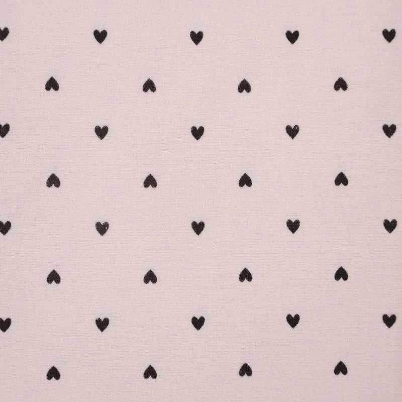 Une flanelle de coton à motifs cœurs rose tendre, vendue au mètre par Longon Craft France, présente un motif répétitif de petits cœurs noirs - idéal pour la couture douillette, le quilting et les projets de couture créatifs.