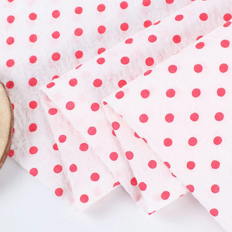 Le Seersucker à pois au mètre de Longan Craft France est un seersucker de coton blanc léger et aéré, à pois rouges et aux bords soigneusement pliés, parfait pour les costumes vintage et les projets de couture créatifs.