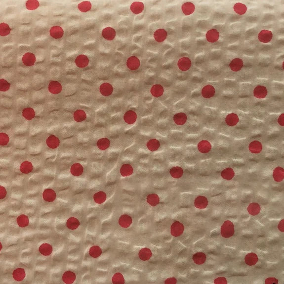 Un gros plan du Seersucker à pois au mètre de Longan Craft France montre un coton imprimé beige texturé avec des points rouges régulièrement espacés et les rides caractéristiques du seersucker, parfait pour les costumes d'époque.