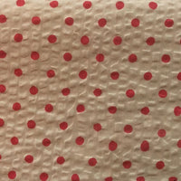 Un gros plan du Seersucker à pois au mètre de Longan Craft France montre un coton imprimé beige texturé avec des points rouges régulièrement espacés et les rides caractéristiques du seersucker, parfait pour les costumes d'époque.