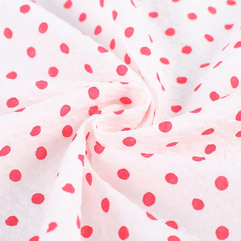 Gros plan sur le seersucker à pois au mètre de Longan Craft France, un tissu léger en coton seersucker avec des pois rouges régulièrement espacés, rassemblés au centre en un tourbillon - idéal pour les costumes d'époque.