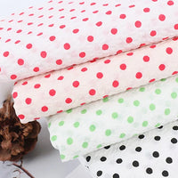 Quatre tissus en coton seersucker de Longan Craft France, à pois vintage rouges, roses, verts et noirs sur fond blanc, sont empilés ; des fleurs séchées reposent à côté de ce tissu léger "Seersucker à pois au mètre".