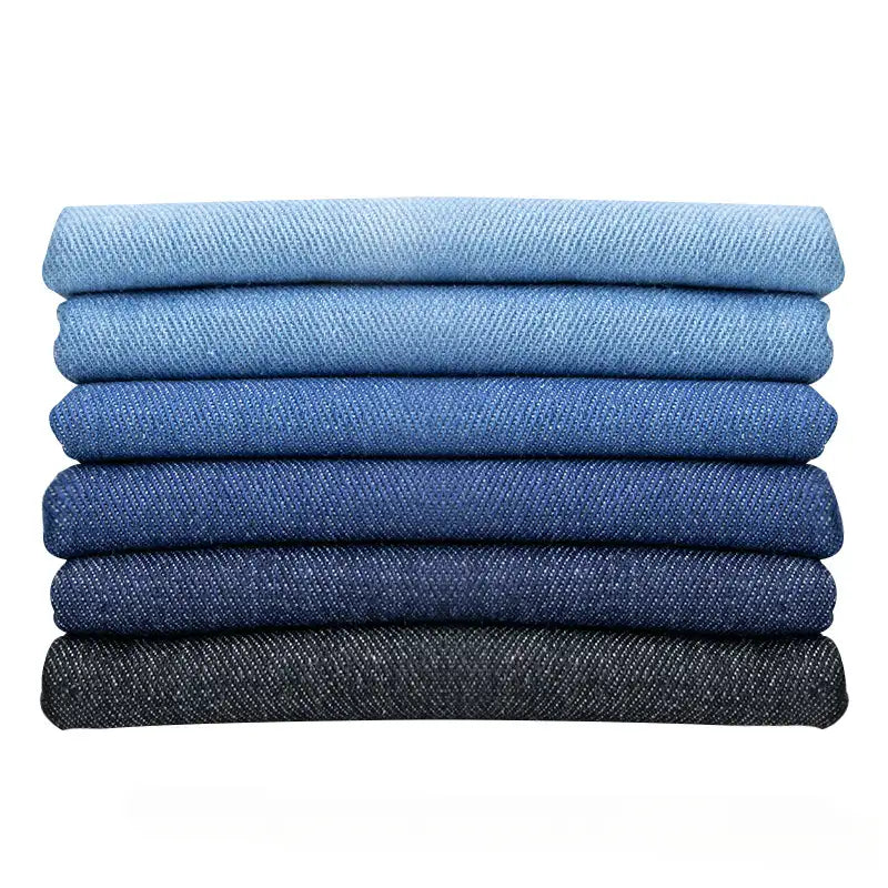Six paires de jeans fabriqués à partir du Tissu en jean extensible au mètre (8 oz denim stretch) de Longan Craft France sont soigneusement empilées dans un dégradé allant du bleu clair au noir sur un fond blanc impeccable.