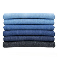 Six paires de jeans fabriqués à partir du Tissu en jean extensible au mètre (8 oz denim stretch) de Longan Craft France sont soigneusement empilées dans un dégradé allant du bleu clair au noir sur un fond blanc impeccable.