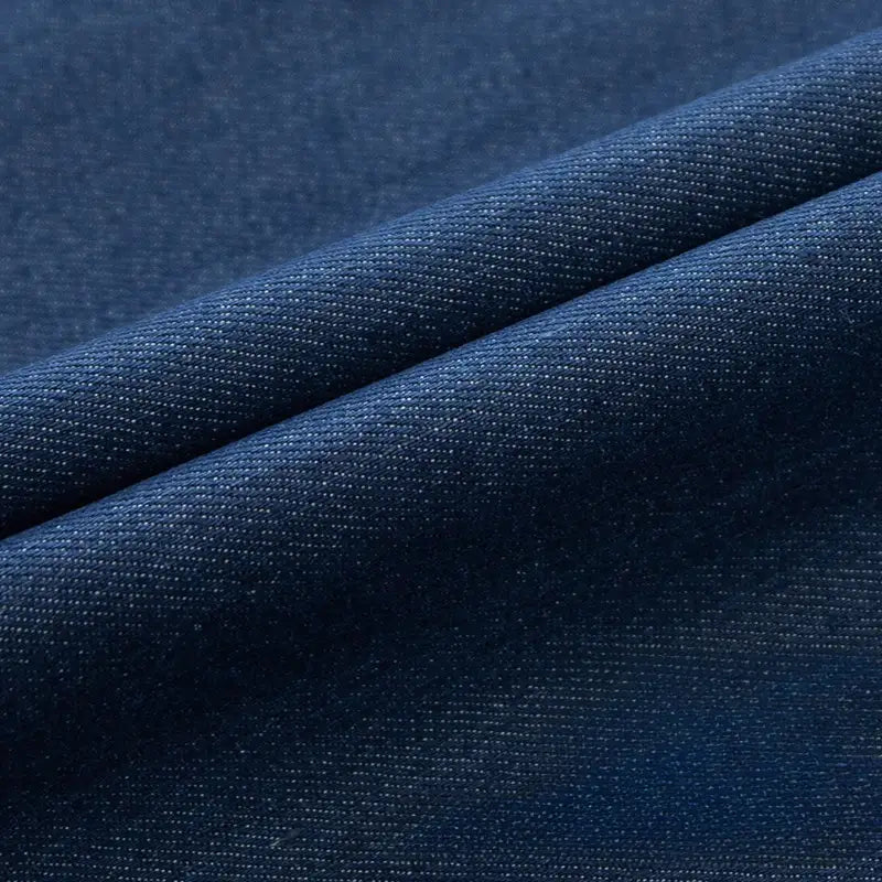 Un gros plan du tissu en jean extensible au mètre de Longan Craft France met en évidence sa texture tissée et ses plis diagonaux, parfaits pour créer des vêtements et des jeans confortables.