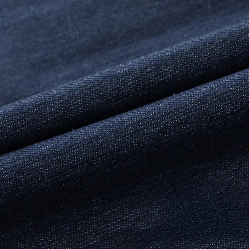Gros plan sur le Tissu en jean extensible au mètre de Longan Craft France, un tissu denim extensible bleu foncé de 8 oz pour vêtements et jeans, montrant son motif de tissage visible et deux plis parallèles diagonaux.