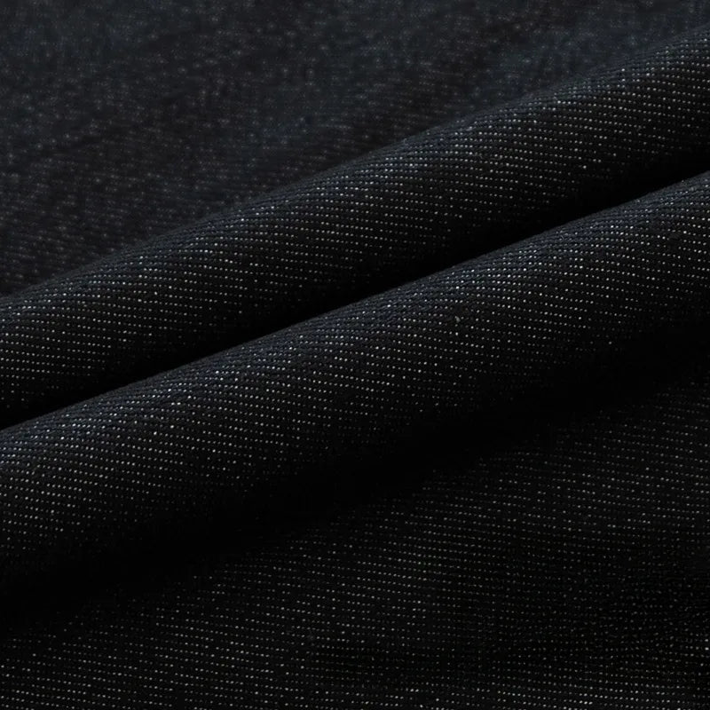 Gros plan sur le Tissu en jean extensible au mètre (8 oz) de Longan Craft France : un denim noir extensible à la texture fine, au tissage visible et à la brillance subtile. Les plis diagonaux soulignent l'élasticité du tissu, idéal pour les jeans et les vêtements.