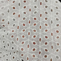 Gros plan sur le Voile de coton brodé au mètre de Longan Craft France : tissu blanc avec une délicate broderie florale ajourée, créant une texture transparente semblable à de la dentelle - parfait pour les robes, la couture et la décoration d'intérieur.