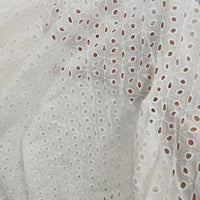 Gros plan sur le "Voile de coton brodé au mètre" de Longan Craft France : un voile blanc avec une broderie florale ajourée, une texture légère et de légers plis. Idéal pour les robes, les projets de couture et la décoration intérieure.