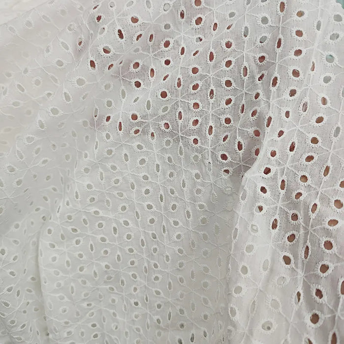Gros plan sur le "Voile de coton brodé au mètre" de Longan Craft France : un voile blanc avec une broderie florale ajourée, une texture légère et de légers plis. Idéal pour les robes, les projets de couture et la décoration intérieure.