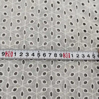 Un mètre ruban en centimètres (20-34) est posé sur le voile de coton brodé au mètre de Longan Craft France, un tissu blanc avec une broderie florale ajourée, idéal pour les peignoirs, la couture et la décoration d'intérieur.