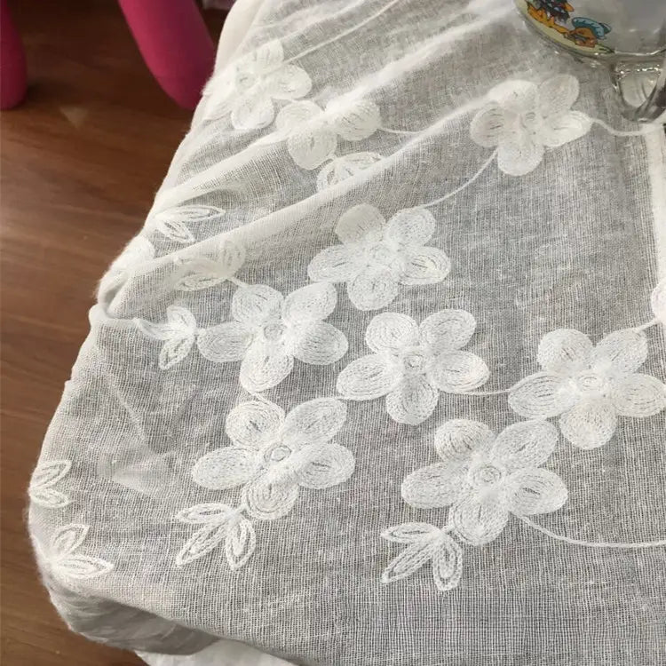 Gros plan sur le tissu brodé floral en gaze de lin au mètre de Longan Craft France en gris clair, montrant une broderie florale blanche avec des grappes de fleurs et de feuilles - idéal tissu naturel et transparent pour vêtements d'été.