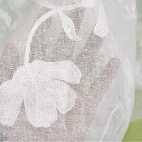 Gros plan sur le Tissu brodé floral en gaze de lin au mètre de Longan Craft France, mettant en valeur son lin naturel et transparent avec une délicate broderie de feuilles et de pétales sur un fond vert clair et beige légèrement flou.