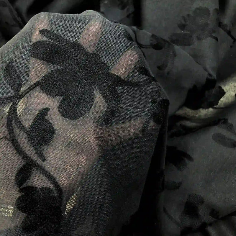 Une main apparaît sous le Tissu brodé floral en gaze de lin au mètre de Longan Craft France, un tissu de lin naturel et transparent pour l'habillement qui met en valeur le contour de la main grâce à un élégant motif floral.