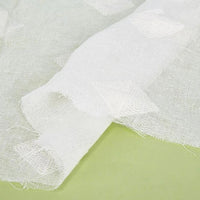 Gros plan sur le Tissu brodé floral en gaze de lin au mètre de Longan Craft France, un tissu de lin naturel semi-transparent à la texture visible, présenté à plat sur une surface vert clair - parfait pour les projets de vêtements.