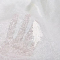 Une main sous le tissu brodé floral en gaze de lin au mètre de Longan Craft France révèle sa texture de lin fine et transparente et sa broderie délicate en forme de feuille, parfaite pour les vêtements d'été naturels.