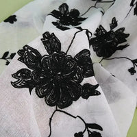 Gros plan sur le tissu brodé floral en gaze de lin au mètre de Longan Craft France : un tissu de lin blanc et transparent avec de grandes broderies florales noires - un textile naturel idéal pour les vêtements et les robes d'été.