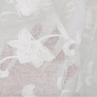 Gros plan sur le Tissu brodé floral en gaze de lin au mètre de Longan Craft France, un tissu de lin naturel et transparent orné de fleurs et de vignes délicatement brodées en blanc. Le tissu transparent laisse transparaître l'arrière-plan.