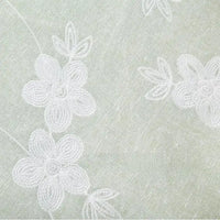 Gros plan sur le "Tissu brodé floral en gaze de lin au mètre" de Longan Craft France - un tissu de lin naturel et transparent qui présente une délicate broderie florale blanche avec des fleurs et des feuilles soulignées pour un aspect texturé.