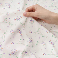A hand holds Tissu mousseline à fleurs au mètre de Longan Craft France : une mousseline polyester imprimée, légère et translucide, ornée d'un délicat motif floral coloré, idéale pour confectionner des vêtements.