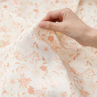 Une main pince un morceau de tissu mousseline à fleurs au mètre de Longan Craft France. Cette mousseline de polyester légère et translucide séduit par son imprimé floral délicat, idéal pour la confection de vêtements.