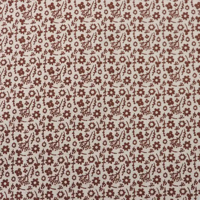 Un gros plan de la Flanelle de coton fleurie au mètre de Longan Craft France montre un motif floral automnal répétitif avec de petites fleurs et feuilles brunes sur fond crème, parfait pour coudre des robes, des vêtements et des travaux manuels.