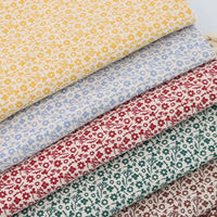 Quatre pièces de "Flanelle de coton fleurie au mètre" de Longan Craft France, présentant des imprimés floraux d'automne colorés sur du coton flanelle blanc, sont soigneusement empilées - idéales pour coudre des robes, des vêtements et des projets créatifs.