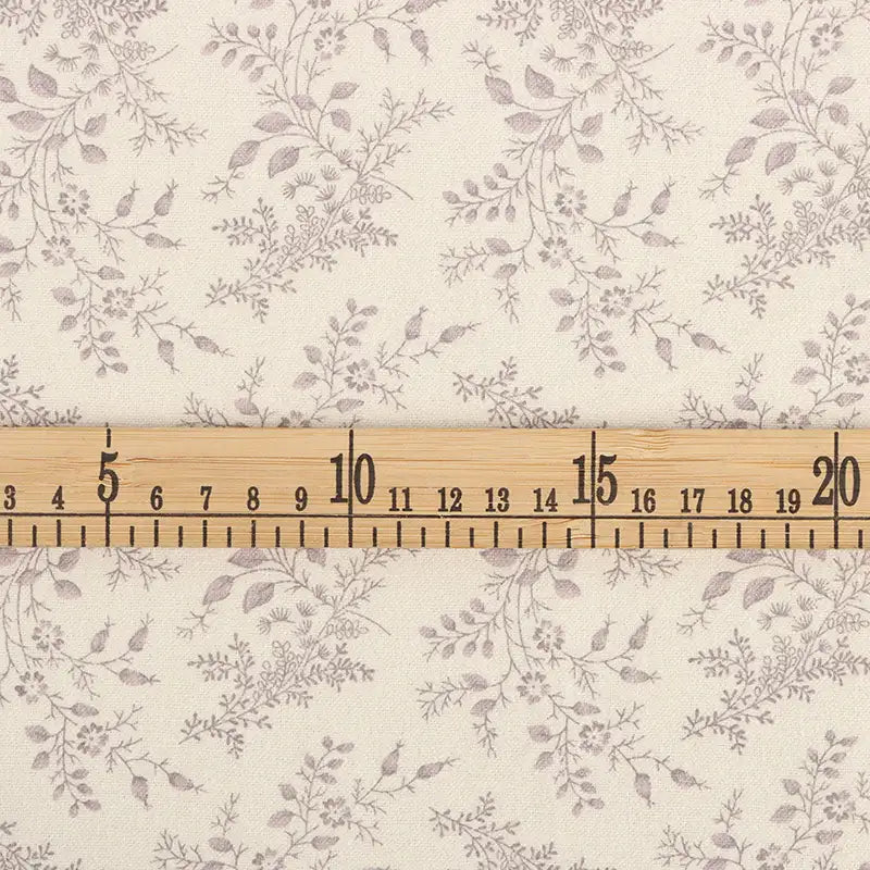 Une règle en bois (3-21 cm) est posée sur la Flanelle de coton fleurie au mètre de Longan Craft France, une flanelle de couleur crème avec un motif floral gris clair, idéale pour les vêtements d'hiver, la couture et les projets créatifs.