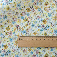 Une règle en bois est posée sur la popeline de coton à fleurs de Longan Craft France, un tissu floral 100 % coton. L'échelle centimétrique montre le charmant imprimé, idéal pour le quilting, les nappes, les robes et les chemises.