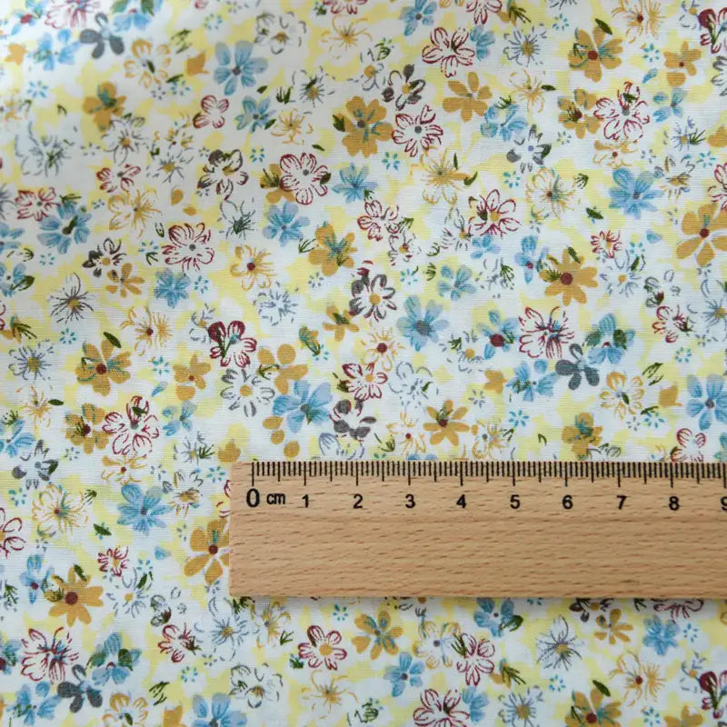Une règle en bois est posée sur la popeline de coton à fleurs de Longan Craft France, un tissu floral 100 % coton. L'échelle centimétrique montre le charmant imprimé, idéal pour le quilting, les nappes, les robes et les chemises.