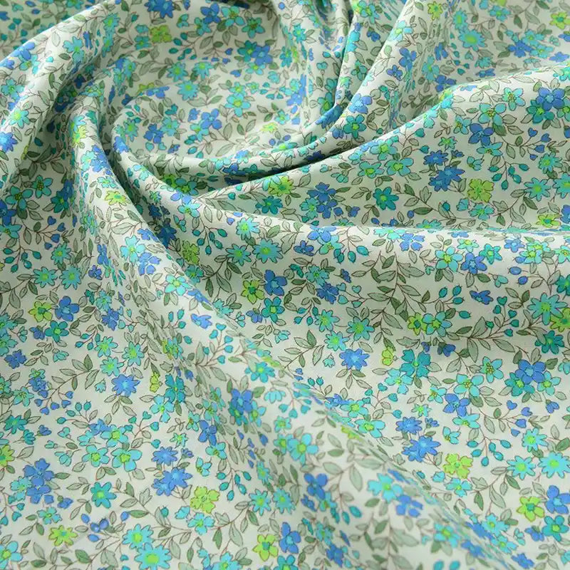 Gros plan sur Popeline de coton à fleurs au mètre de Longan Craft France, un tissu doux 100 % coton à l'imprimé floral bleu et vert, délicatement froncé pour mettre en valeur sa texture naturelle - parfait pour le quilting, les nappes, les robes et les chemises.