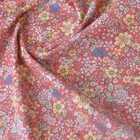 Un gros plan de Popeline de coton à fleurs au mètre de Longan Craft France montre son imprimé floral dense en jaune, rouge, rose et blanc sur un tissu popeline doux 100% coton, légèrement froissé - idéal pour le quilting, les langes, les peignoirs et les chemises.