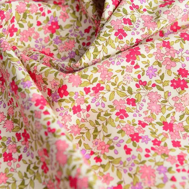 Gros plan sur la "Popeline de coton à fleurs" de Longan Craft France, une popeline douce 100% coton avec de petites fleurs roses, rouges et violettes sur un fond clair. Idéal pour le quilting, les nappes, les robes ou les chemises. Le tissu est légèrement froissé.