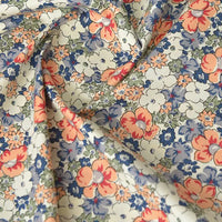 Gros plan sur la Popeline de coton à fleurs au mètre de Longan Craft France, montrant son imprimé floral doux 100 % coton avec des fleurs orange, bleues et blanches et des feuilles vertes. Le tissu légèrement torsadé met en valeur sa texture et sa flexibilité pour les projets de couture.