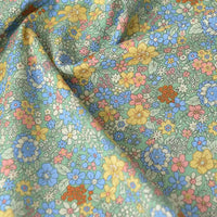 Gros plan sur Popeline de coton à fleurs de Longan Craft France, un tissu doux 100 % coton aux imprimés floraux denses jaunes, bleus, roses et orange sur fond vert clair, idéal pour le quilting, les nappes, les robes et les chemises.