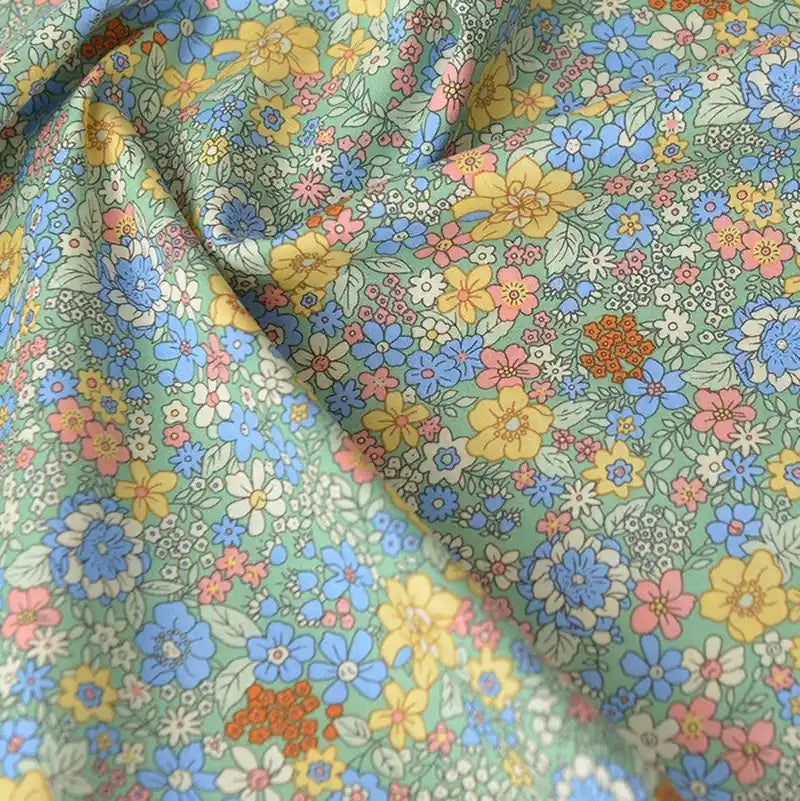 Gros plan sur Popeline de coton à fleurs de Longan Craft France, un tissu doux 100 % coton aux imprimés floraux denses jaunes, bleus, roses et orange sur fond vert clair, idéal pour le quilting, les nappes, les robes et les chemises.