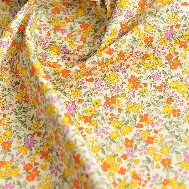 Gros plan sur Popeline de coton à fleurs de Longan Craft France, un tissu doux 100 % coton avec un imprimé floral coloré - fleurs jaunes, orange, violettes et rouges avec des feuilles vertes - idéal pour le quilting, les nappes, les robes et les chemises.