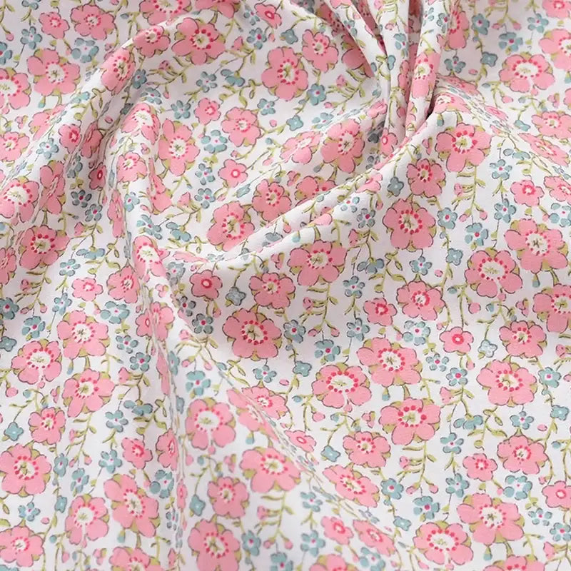 Popeline de coton à fleurs au mètre de Longan Craft France : tissu 100 % coton doux, imprimé floral avec petites fleurs roses et feuilles vertes sur fond blanc, légèrement froissé. Idéal pour quilting, nappes, robes et chemises.