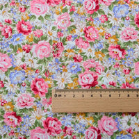 Une règle en bois est posée sur la Popeline de coton à fleurs de Longan Craft France, un tissu doux 100 % coton à l'imprimé floral vibrant, idéal pour le quilting, les nappes, les robes et les chemises. La règle est marquée en centimètres et en millimètres.