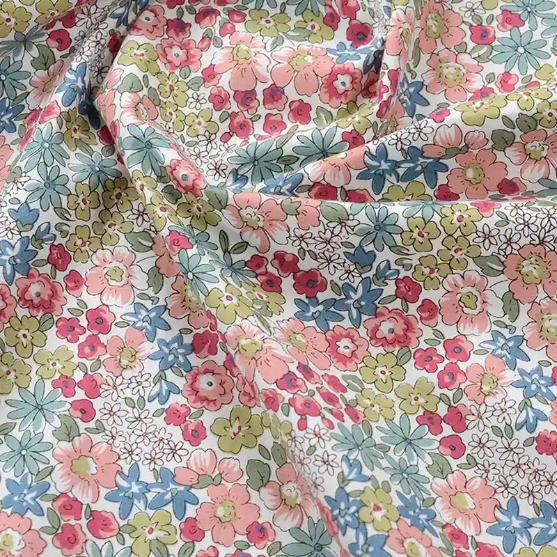 Gros plan sur la Popeline de coton à fleurs au mètre de Longan Craft France, un tissu floral 100 % coton avec des fleurs roses, rouges, bleues et jaunes sur un fond clair. Le tissu doux est légèrement froissé et idéal pour le quilting et la confection de vêtements.