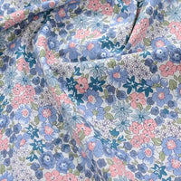 Gros plan sur la Popeline de coton à fleurs au mètre de Longan Craft France, un tissu floral doux 100 % coton avec des fleurs bleues, roses et violettes sur fond blanc, idéal pour le quilting, les nappes, les robes et les chemises.