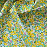Gros plan sur la Popeline de coton à fleurs de Longan Craft France, un tissu doux 100% coton avec un imprimé floral jaune, vert, bleu et rose sur un fond clair. Idéal pour le quilting, les nappes, les robes et les chemises ; drapé délicatement avec des plis doux.