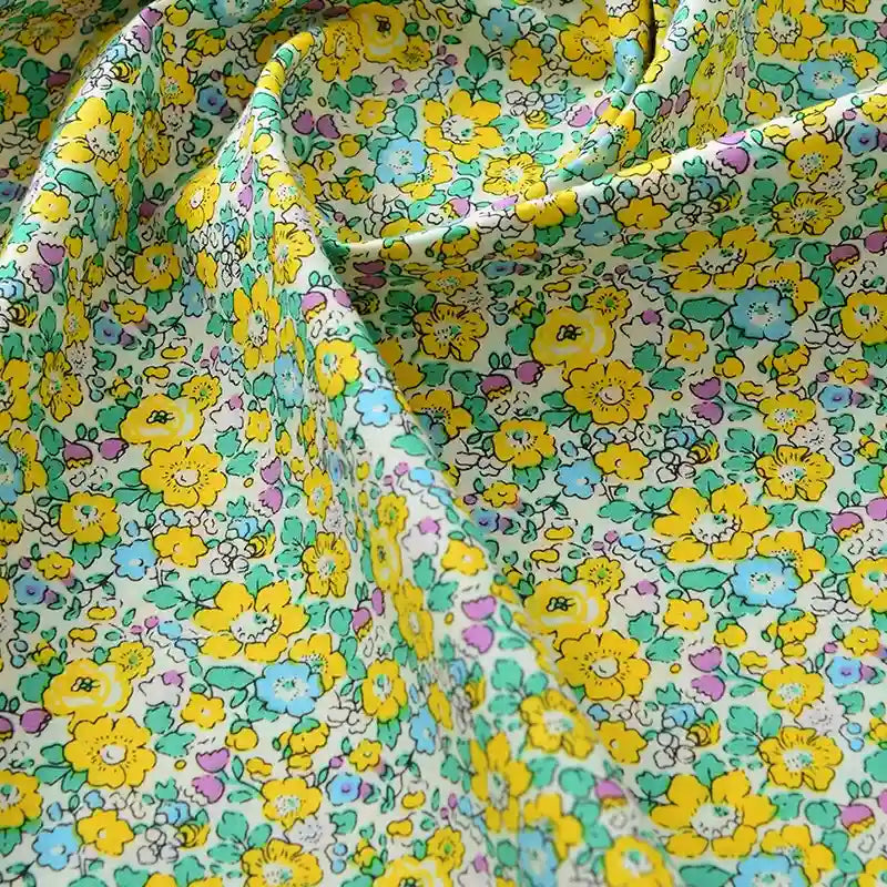 Gros plan sur la Popeline de coton à fleurs de Longan Craft France, un tissu doux 100% coton avec un imprimé floral jaune, vert, bleu et rose sur un fond clair. Idéal pour le quilting, les nappes, les robes et les chemises ; drapé délicatement avec des plis doux.